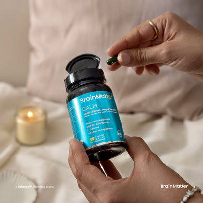 BrainMatter Calm – person holding green capsule from open supplement bottle in relaxed bedroom setting | Balance8 Wellness