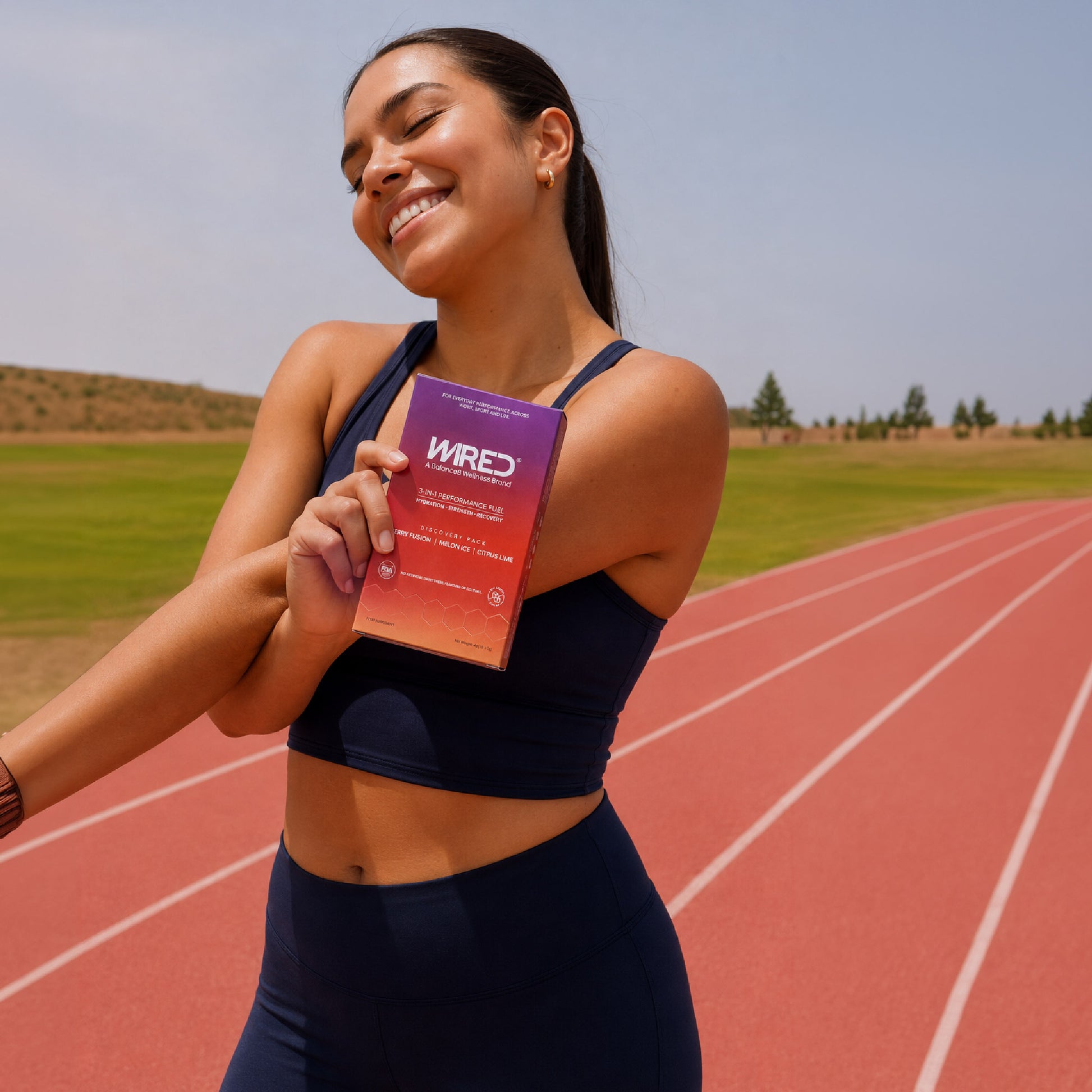 WIRED Discovery Pack – smiling female athlete holding box on running track lifestyle shot | Balance8 Wellness
